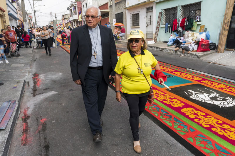 El cardenal Álvaro Ramazzini y un voluntario católico pasan junto a una alfombra de aserrín en la ciudad de Guatemala, el sábado 23 de marzo de 2024. (Foto AP/Moisés Castillo)